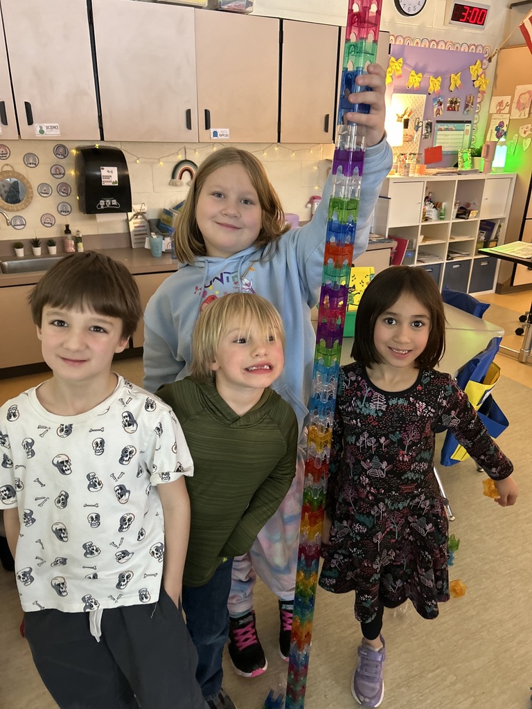 4 students standing in a classroom building a tower looking at the camera smiling