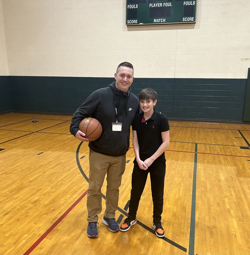 Volunteer holding a basketball posing for a photo with a student inside the gym