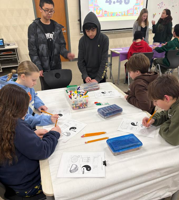 two girls and four boys working at a table with white paper on a cultural art project