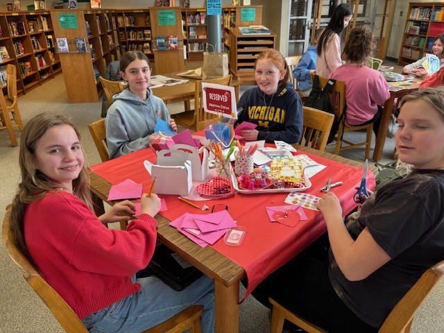 Four students sitting around a table making valentines crafts