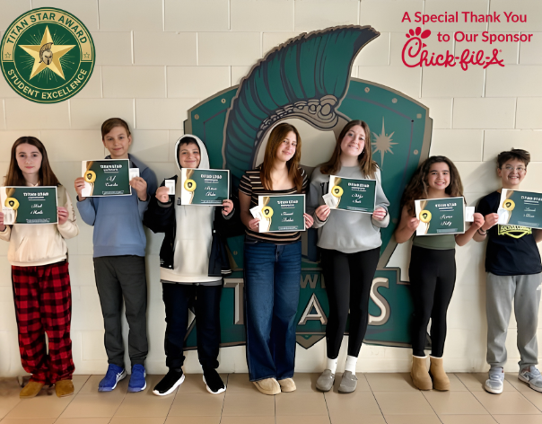 seven students standing in front of a Titan logo holding their Titan Star certificates.