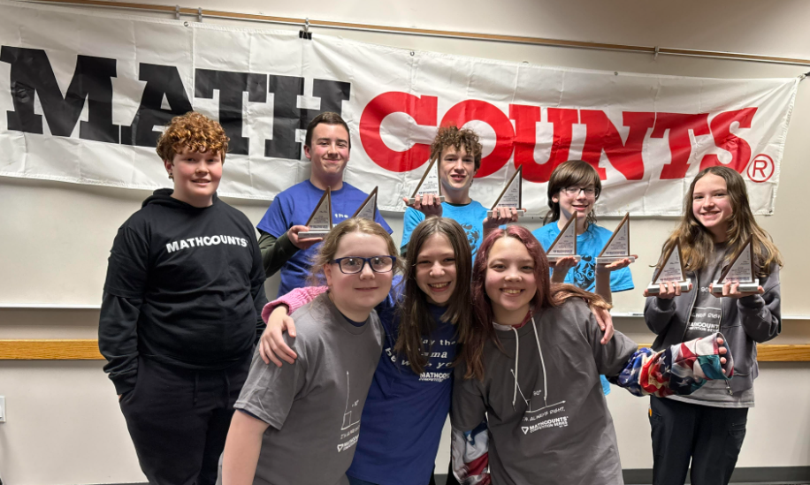 Picture of eight students who participated in Math Counts standing in front of Math Counts banner, four students are holding awards
