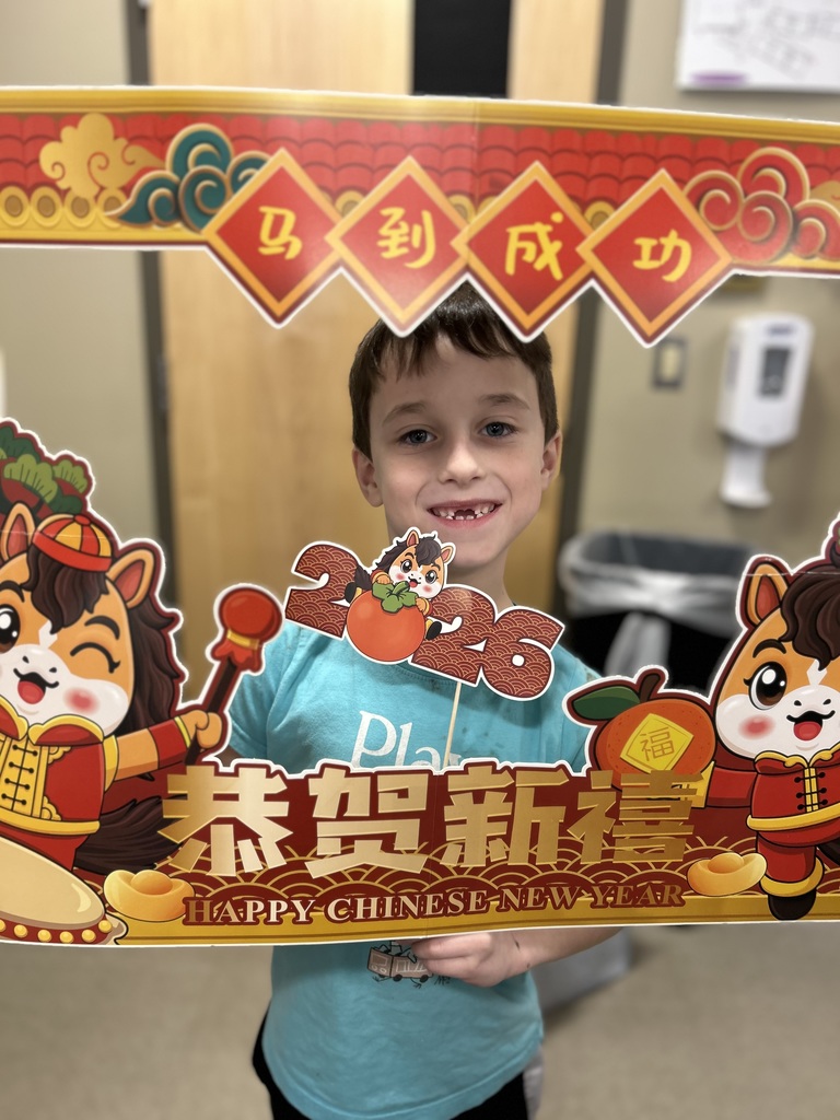 A second grade boy looking through a festive cardboard frame decorated for the Chinese New Year that he is holding.