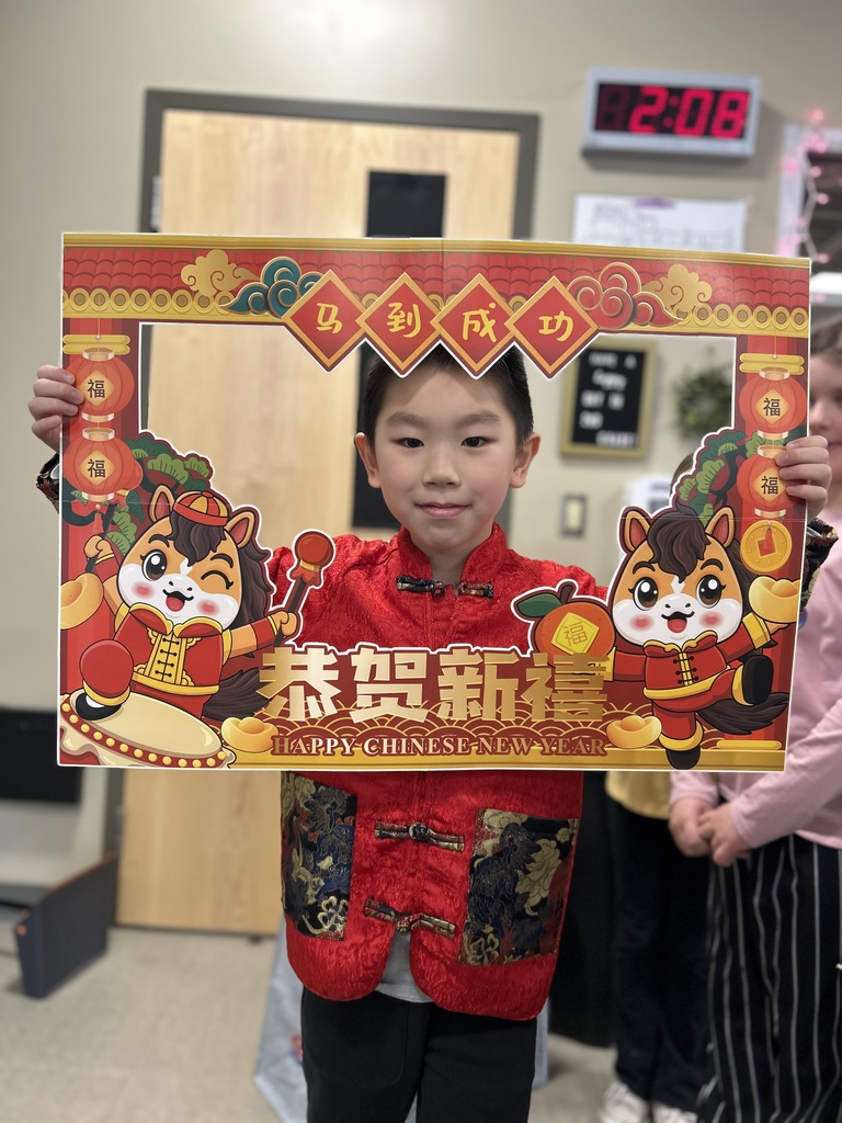 A second grade boy looking through a festive cardboard frame decorated for the Chinese New Year that he is holding.