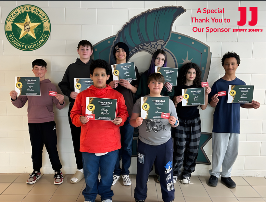 8 students standing in front of the Titan Logo holding their Titan Star certificates