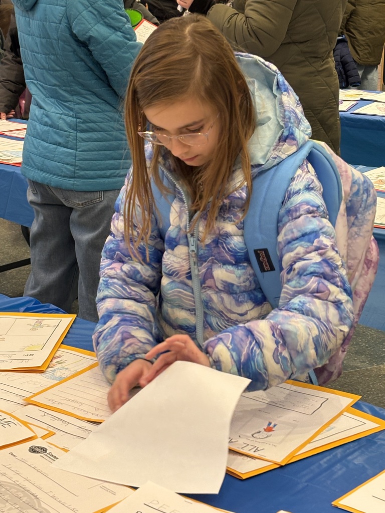 An Eastern female student wearing glasses and a backpack is folding back on page of student writing while reading the next page.