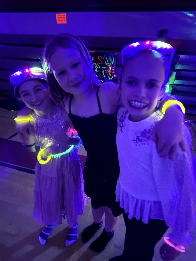 three girls with arms around each other with glow bands around their wrists and waist smiling in the dark gym