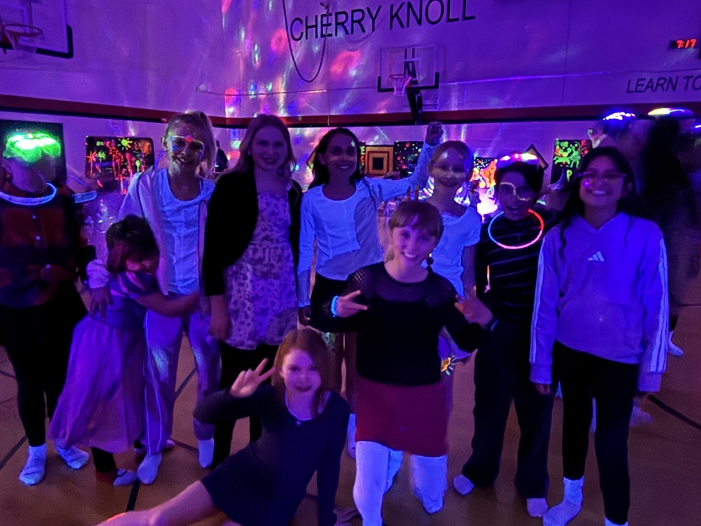 7 students standing 2 students on the ground  and one little girl holding onto a girl with glow lights behind them