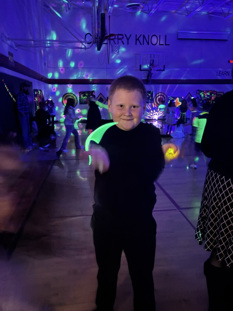 a boy swinging around glow sticks with other people in the background and strobe lights on the wall  in a dark gym