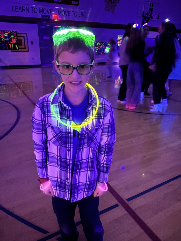 one boy in a dark gym with glowing glasses on his head and a big glow stick necklace