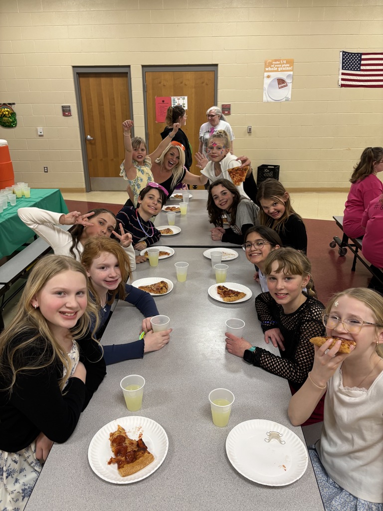eleven students and one adult sitting at a cafeteria table eating pizza