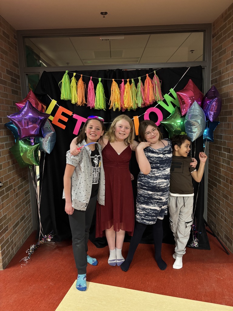 two boys and two girls with arms around each other standing in front of balloons and a sign that says Let it Glow