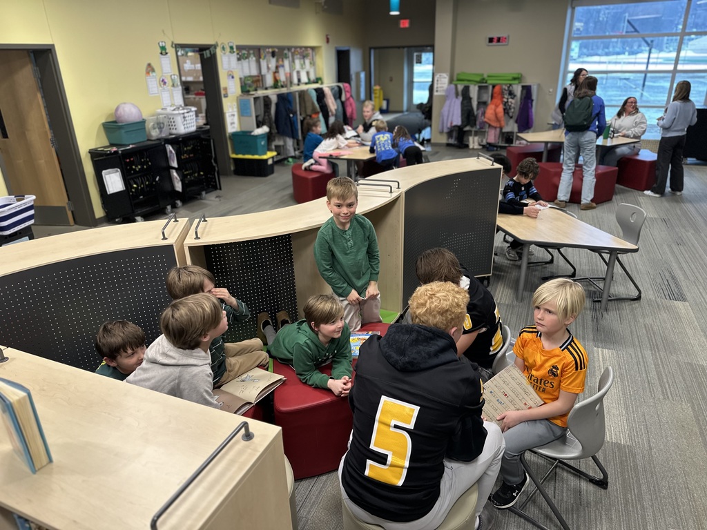 A Traverse City Central football player sits among seven students; the football player is talking to one of the students holding a book.