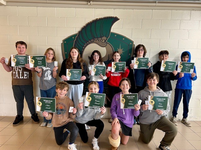 Group of students holding certificates in front of Titan Logo