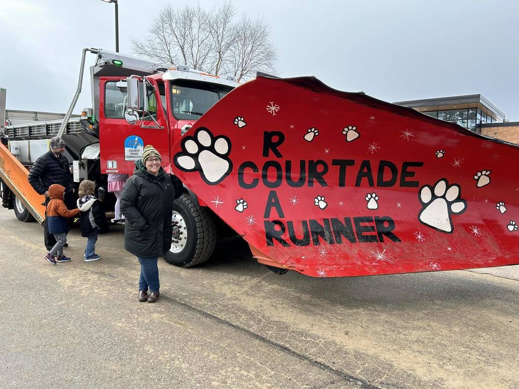 Adults and children standing by a snow plow that has the words Roar Courtade Runner painted on it