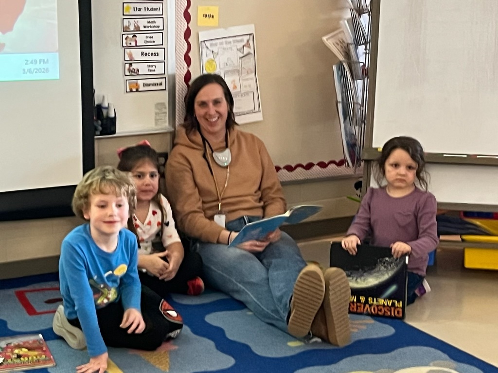 Adult and students sitting on the floor reading a book together