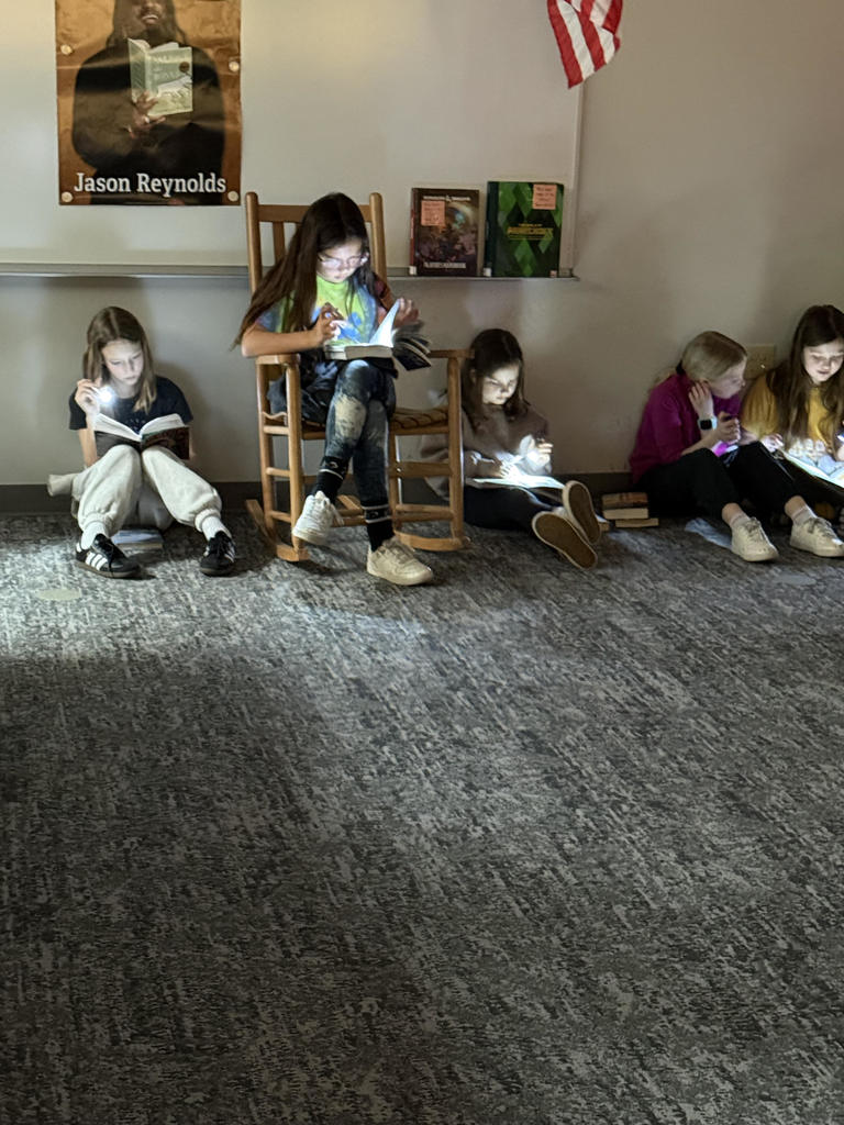 Students reading in the library media center using flashlights to read their book.