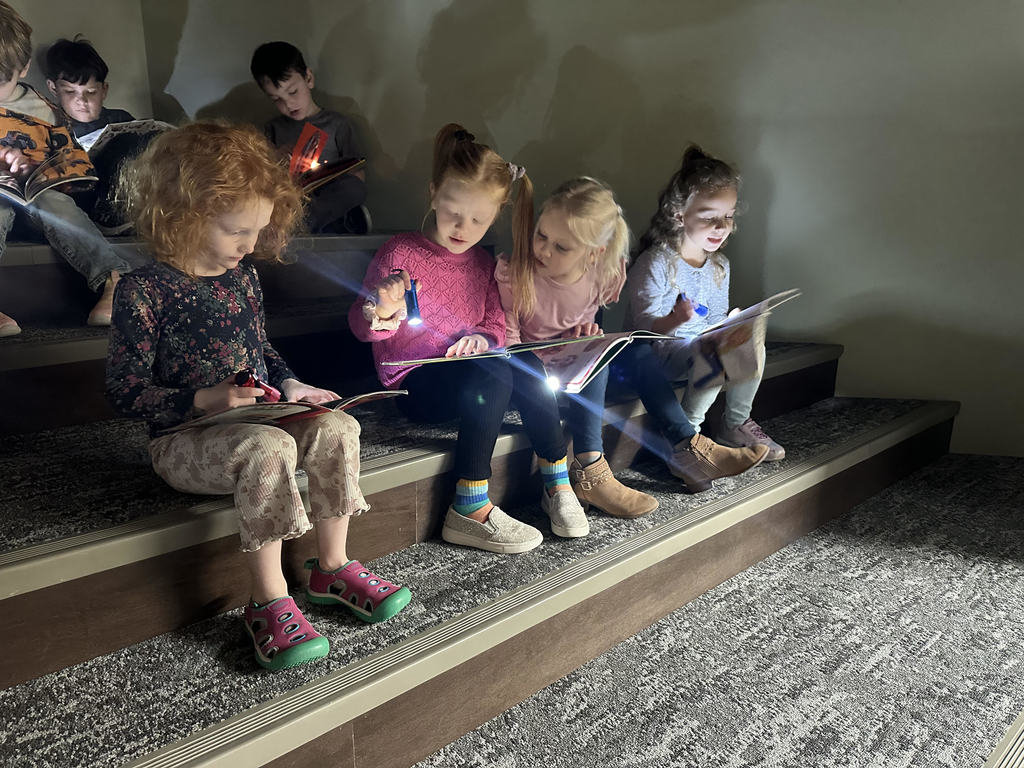 Students reading in the library media center using flashlights to read their book.