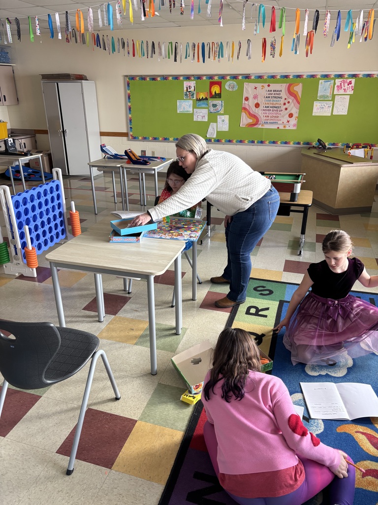 Teacher looking at a board game with a student.  Two other students exploring a board game.  