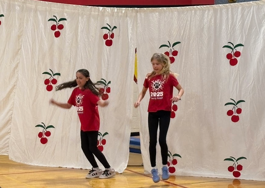 Two girls in matching red "2025" shirts jump in unison during a high-energy dance number.