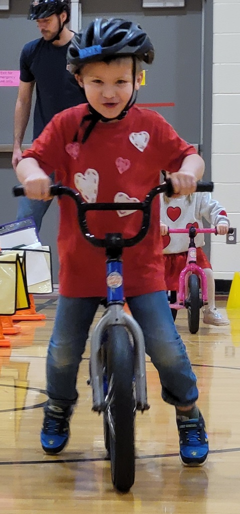 A child in a red shirt decorated with hearts smiles while steering a bike during a Norte session.