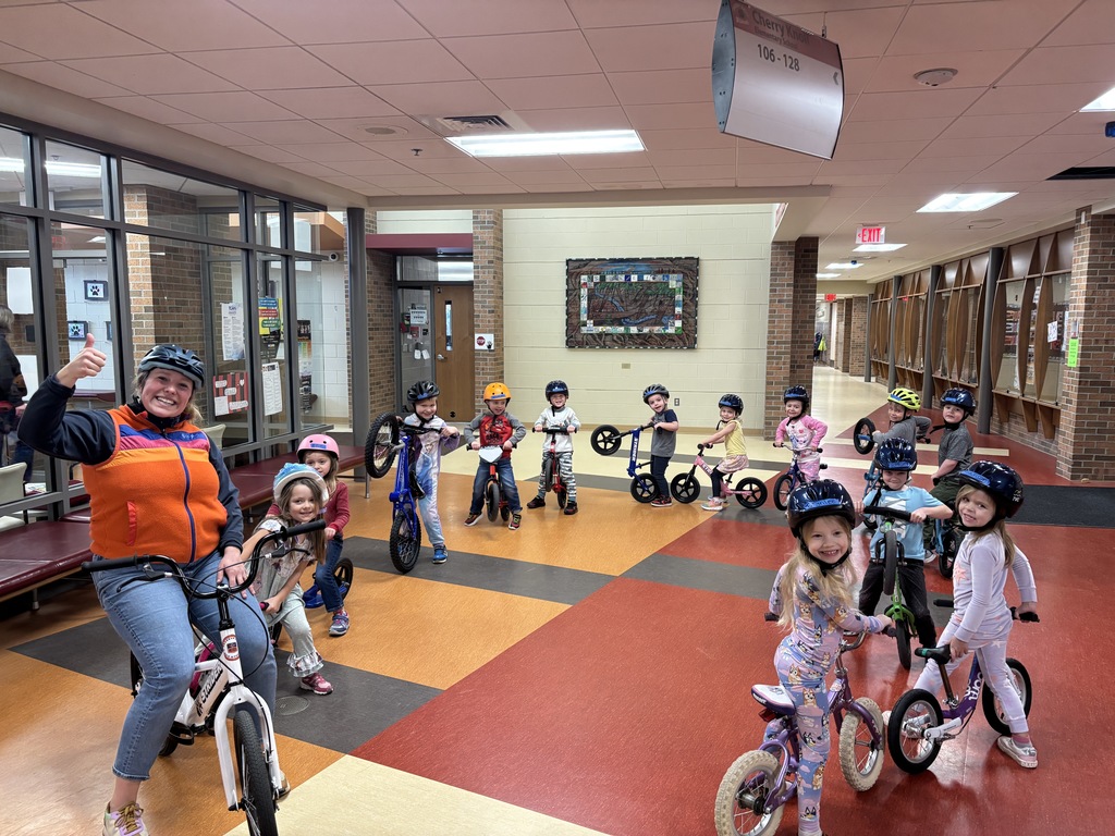 A teacher and a large group of preschoolers pose with their bikes in the Cherry Knoll Elementary hallway.
