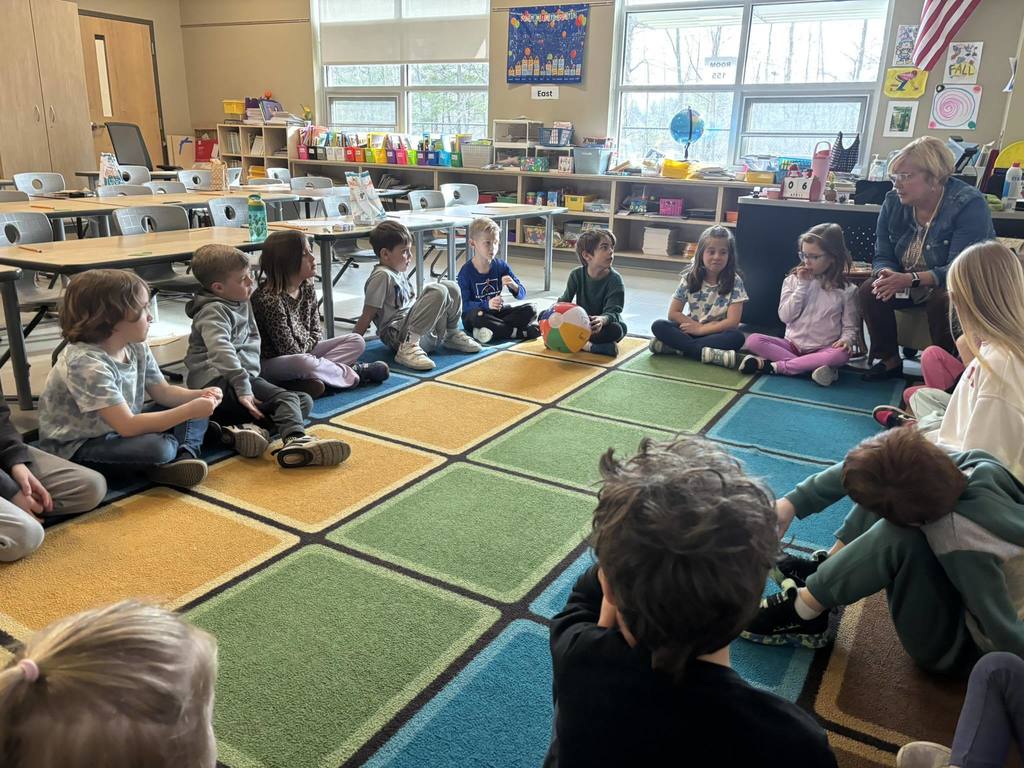 Students sitting on the carpet squares, having a conversation with their teacher.