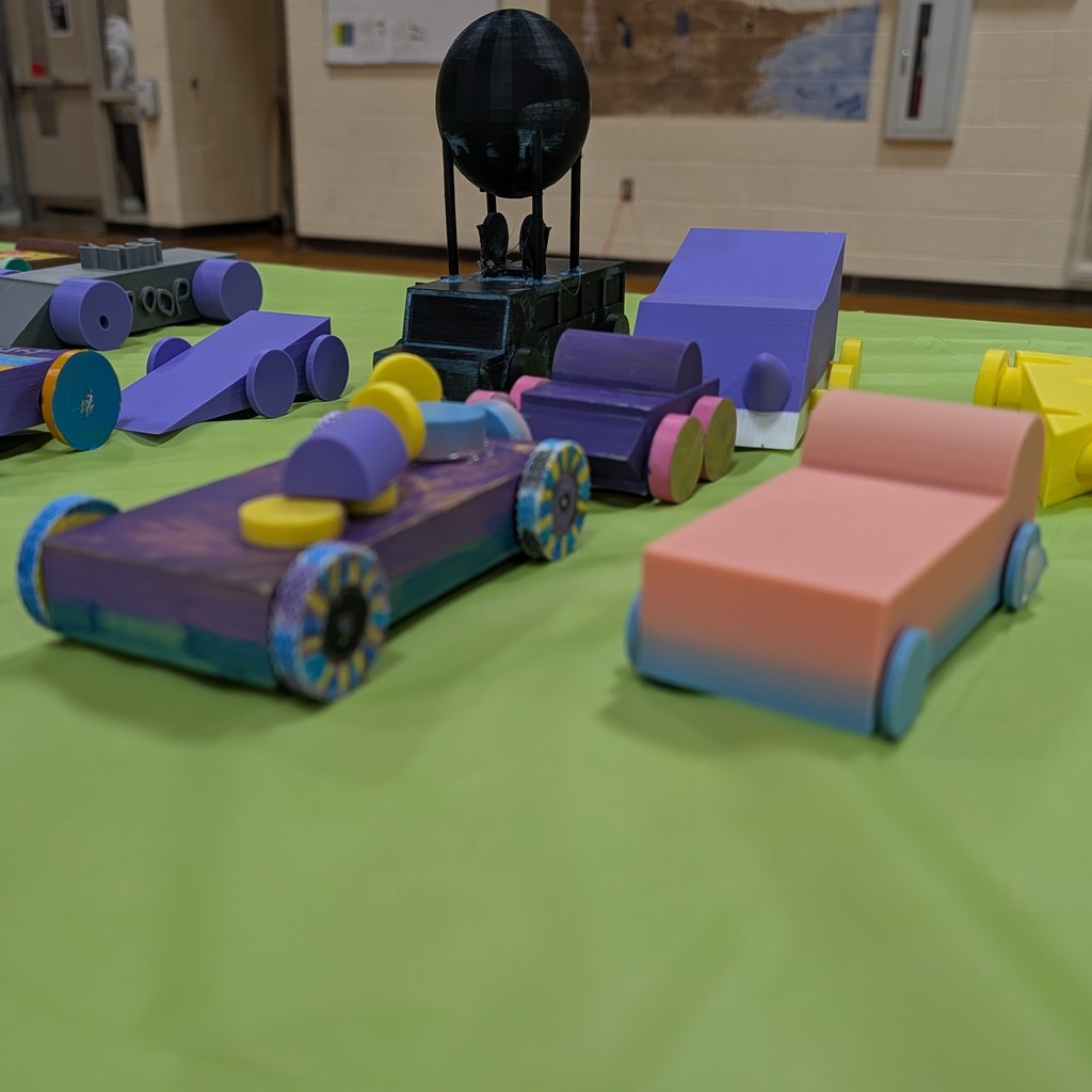 Colorful toy cars and objects on a green table with a wall and a sphere-shaped object in the background.