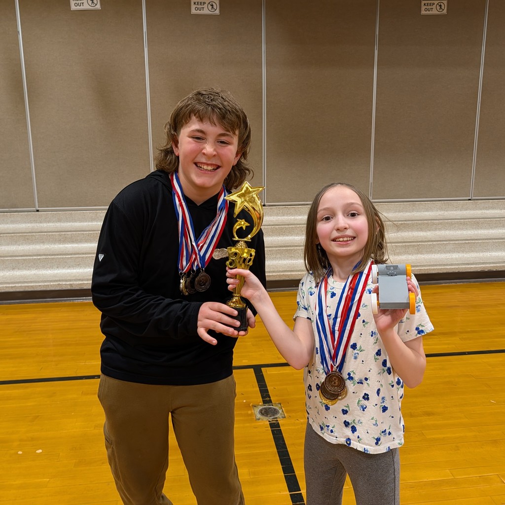 Two kids, a boy and a girl, stand in a gymnasium with medals around their necks.