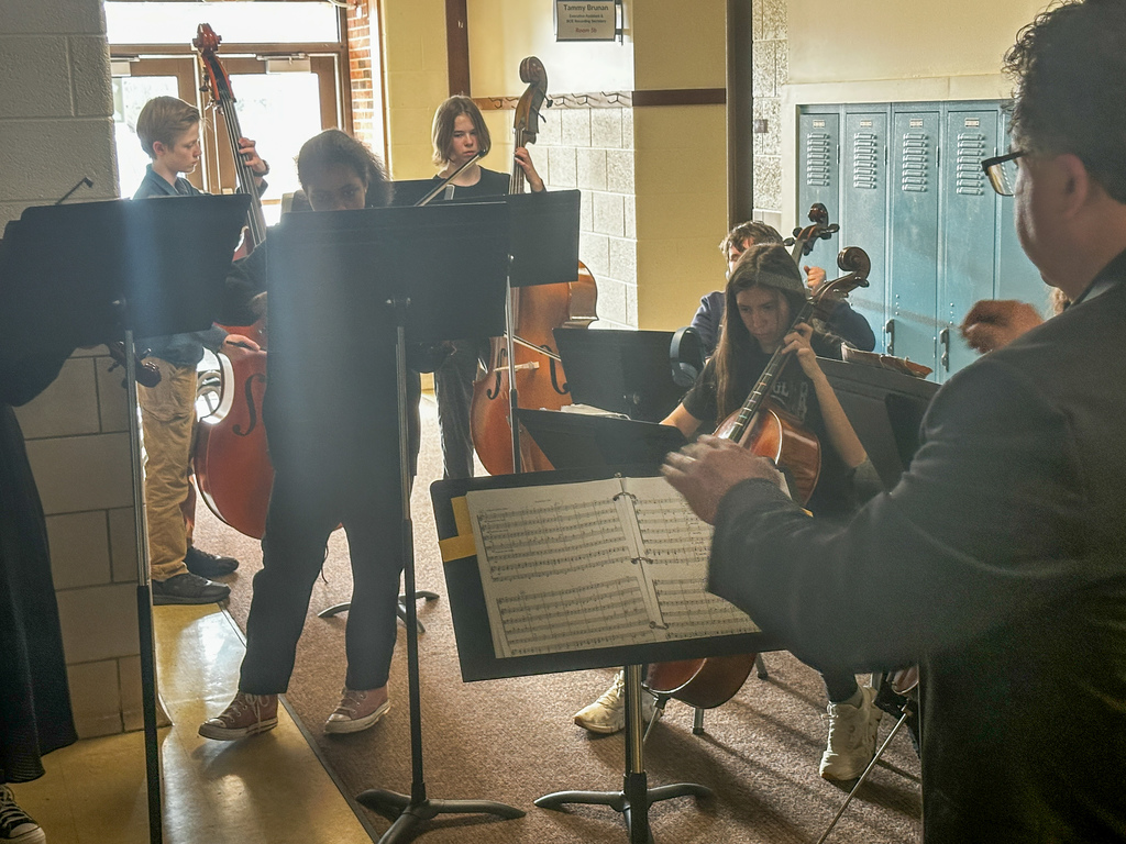 Students playing their string instruments  in the hallway