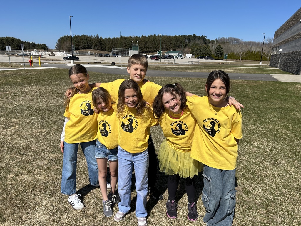 Six children in yellow t-shirts with a duck logo pose for a photo in a grassy area.