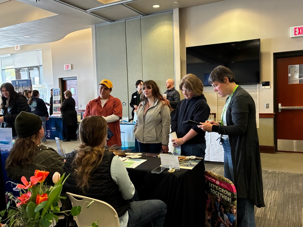 Group of people at a table with a black cloth and flowers, with an exit sign and television on the wall.
