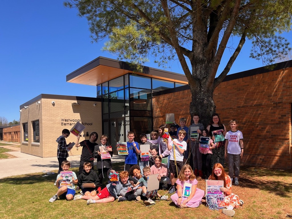 Group of children sitting and standing on grass, holding books, posing for a photo in front of a building.
