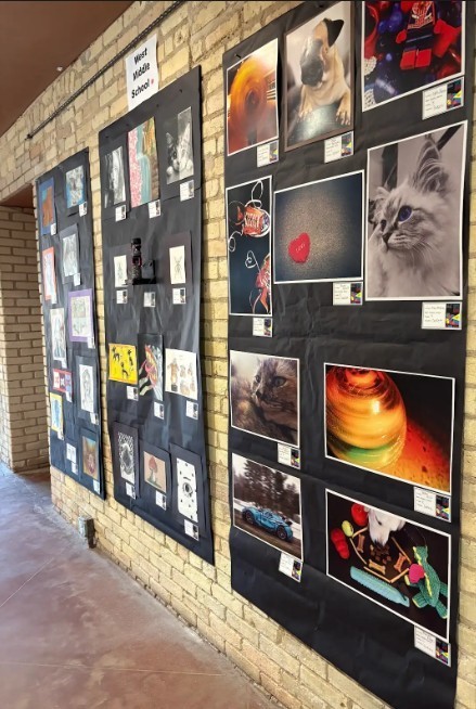 Tan brick wall with large pieces of black paper hanging. Photos taken by WMS students are hanging on the back paper. 