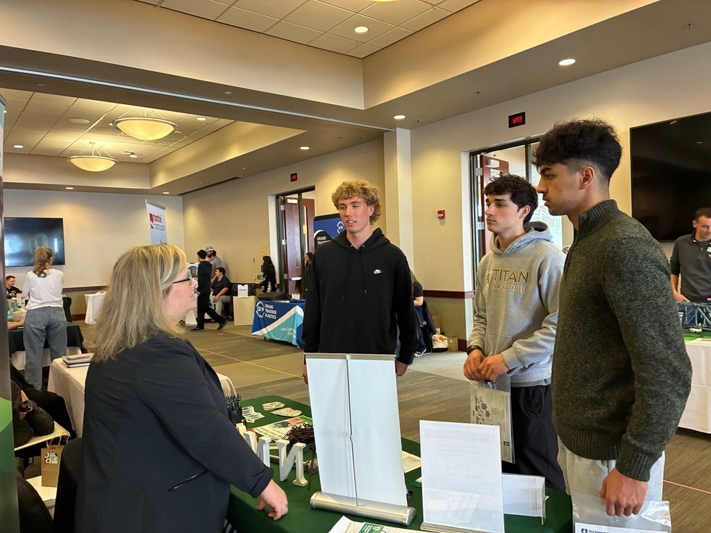 People gather around a table with promotional materials. A woman and three men are engaged in conversation.