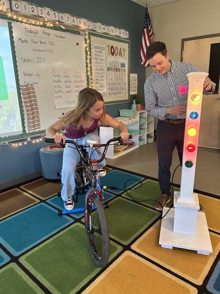 A man and girl in a classroom ride a bike on a stand with a traffic light.