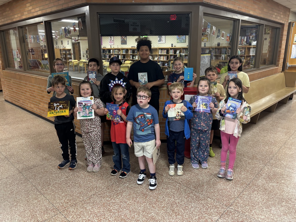 A group of young children poses for a photo in a library, each holding a book.