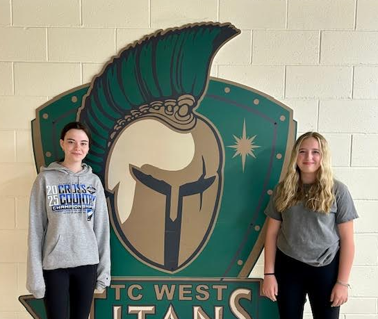 Two students standing in front of the green Titan Logo