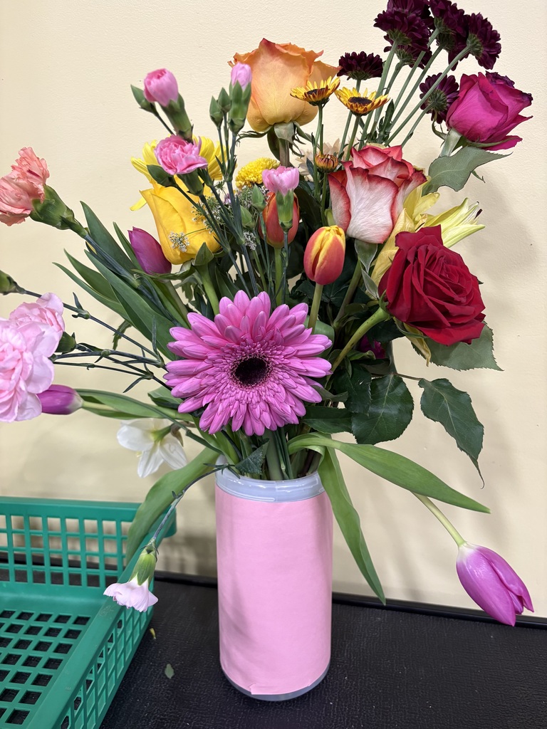 Colorful flowers in a pink vase on a table with a green basket beside it.