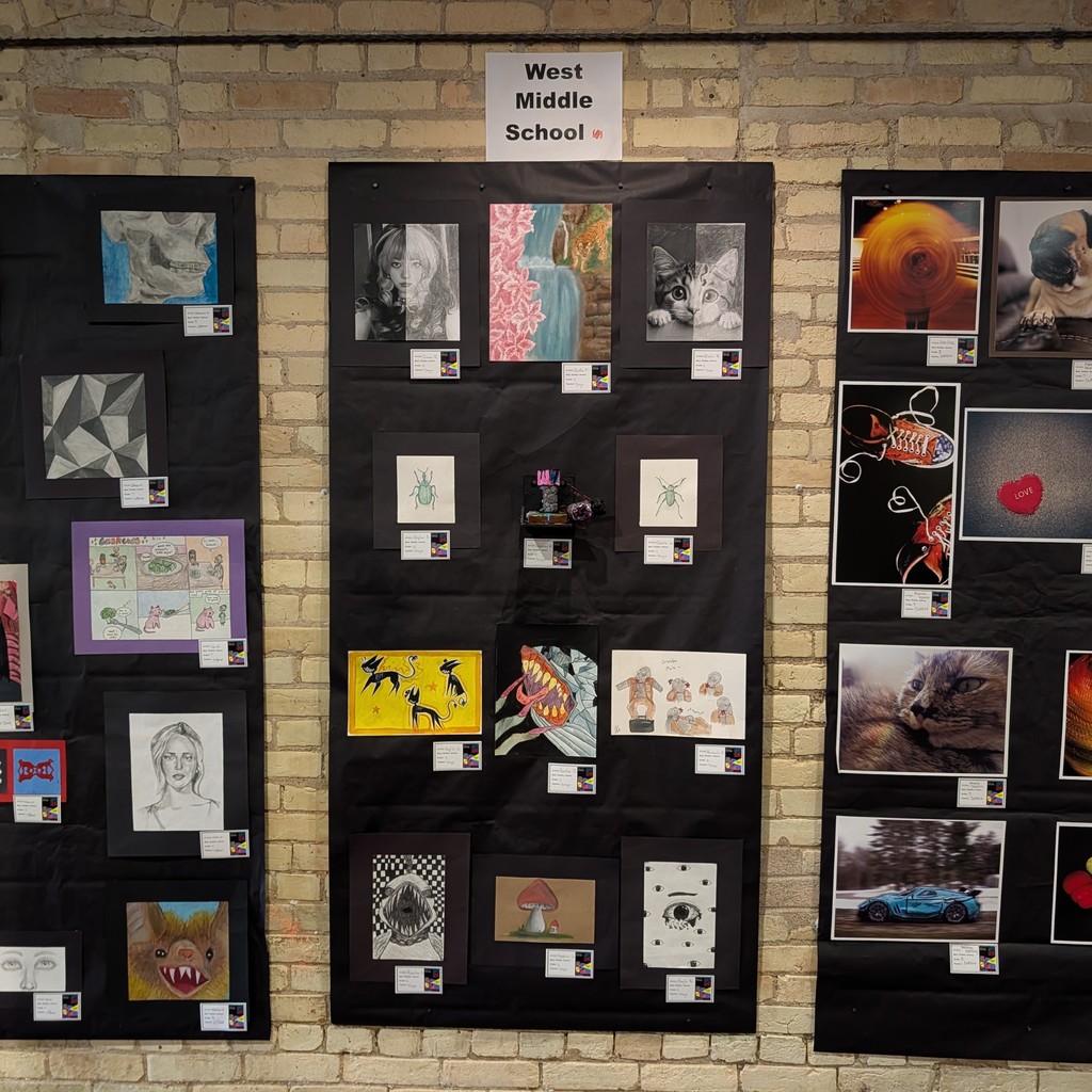 Artworks displayed on three black panels, each with diverse images and colors, against a brick wall.
