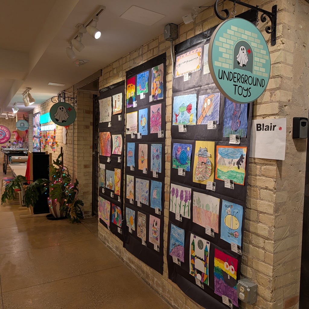 A hallway with brick walls, featuring displayed artworks and a circular sign reading "Underground Toys."