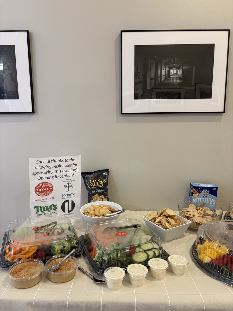 A table with a variety of foods, including salads and dips, displayed in bowls and containers. Two framed pictures hang above.