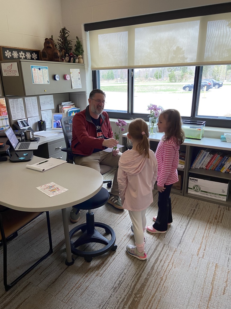 A man in an office chair talks with two children standing next to him.