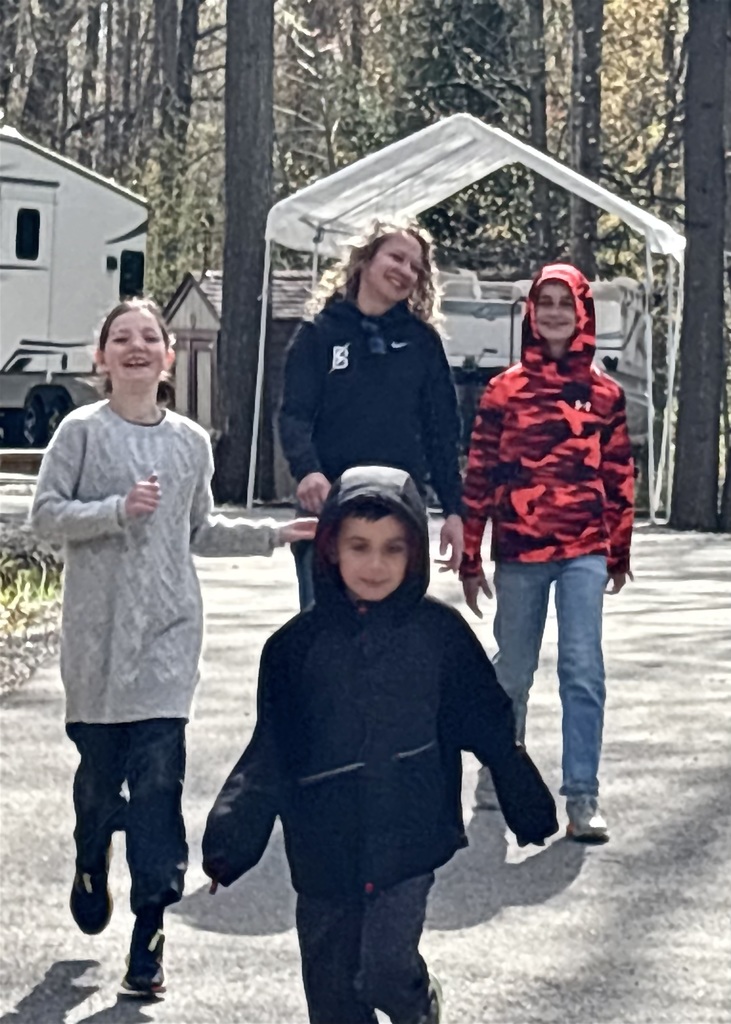 Four people walk on a paved path with trees and a canopy in the background.