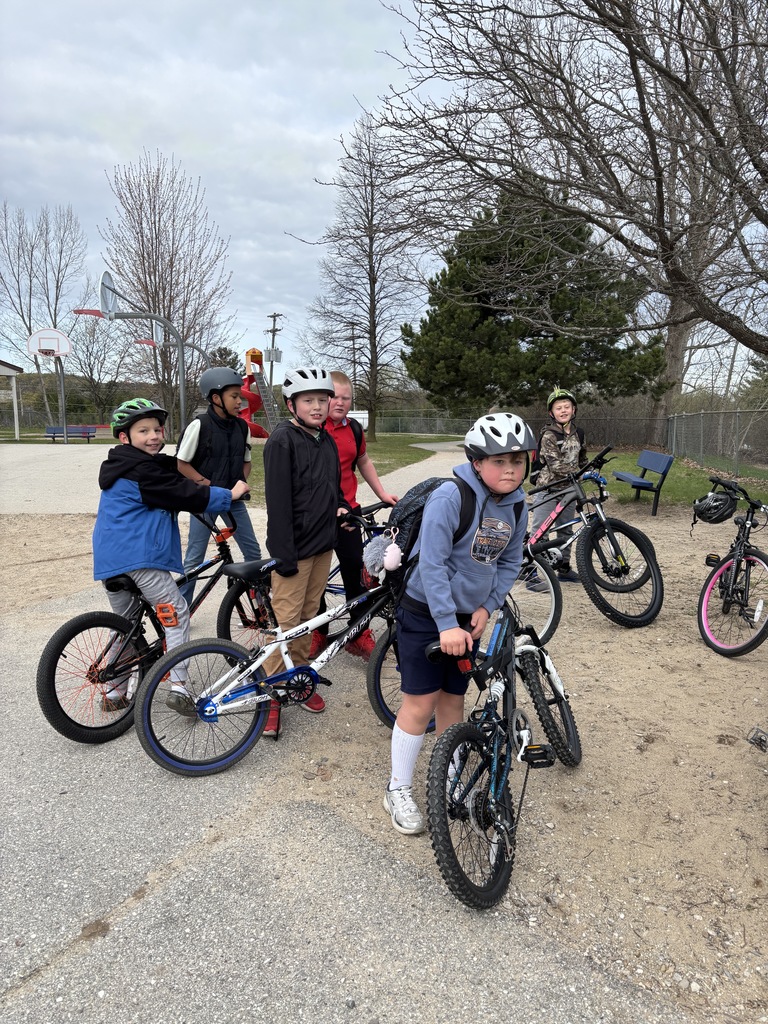 Six children posing with their bikes and helmets in a park next to a picnic table