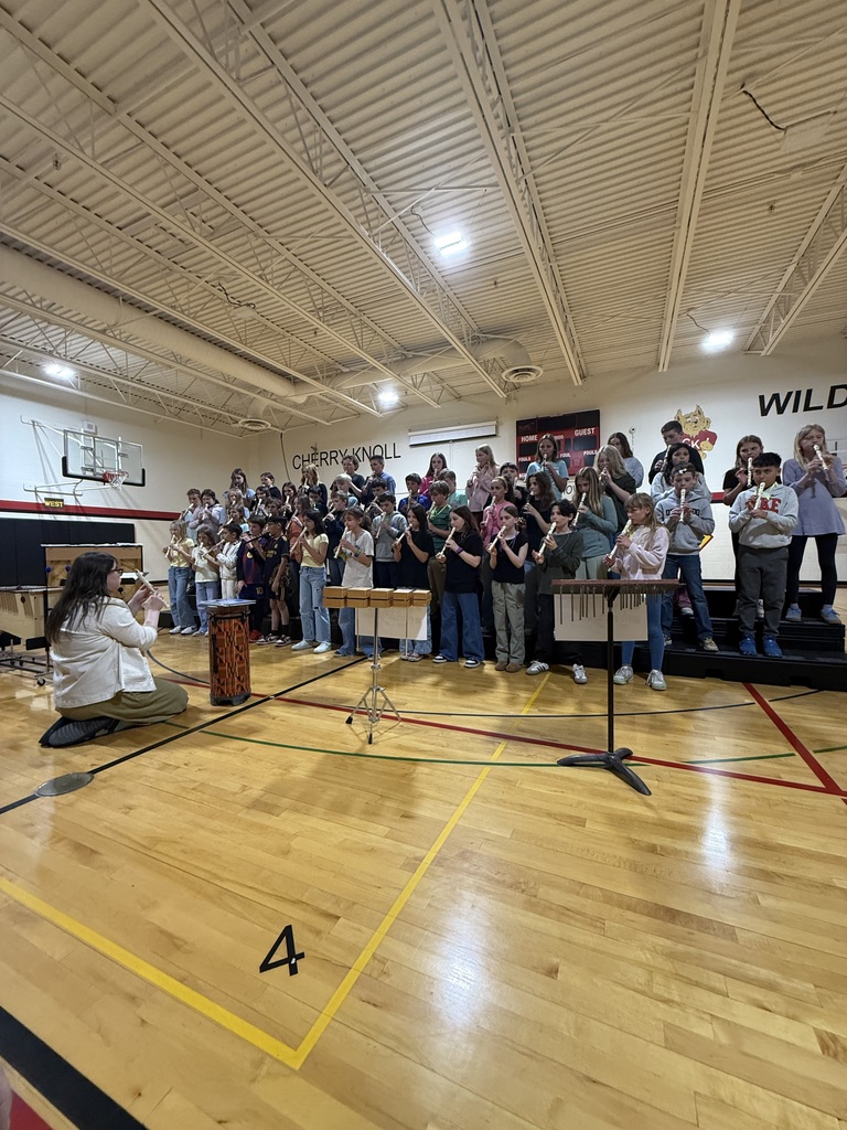 A group of musicians in a gym. A woman plays the flute on the left, with others playing various instruments.