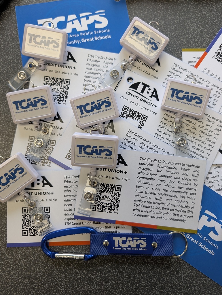 Printed badges with the text "TCAPS" and QR codes on them. A blue carabiner with the text "TCAPS" attached to a document.