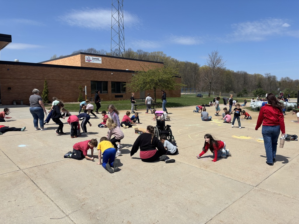 A group of people, including children, are creating art with chalk in a paved area in front of a building.