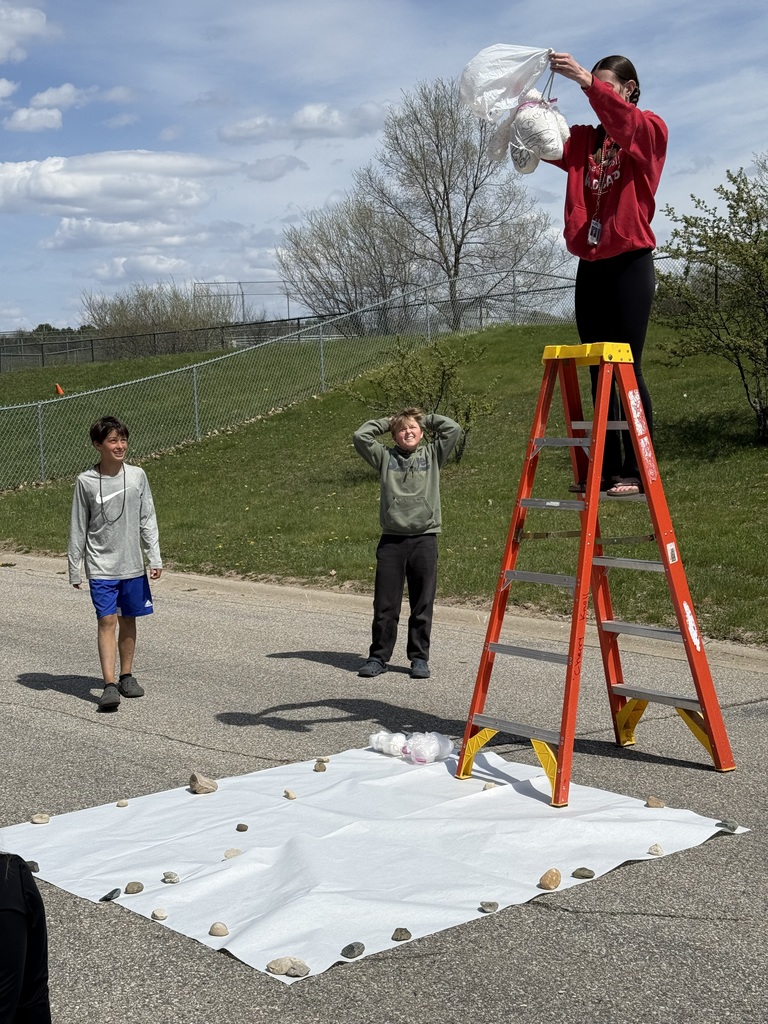 An educator prepares to drop a cushioned egg project from a ladder for a science experiment.