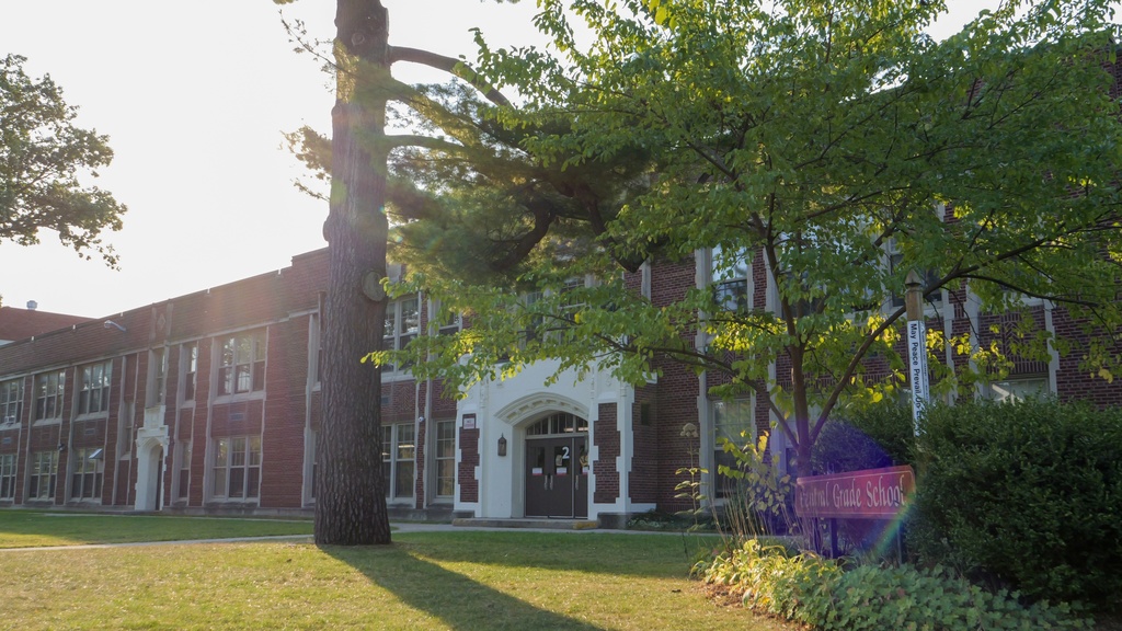 A large brick building with several windows and a white door is surrounded by trees and greenery.